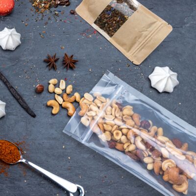 Image montrant un sachet Doypack® transparent rempli de noix et de fruits secs, entouré d'épices, de meringues et d'autres aliments. Le sachet est hermétique et fabriqué en PE/VOH-PE avec une couche d'EVOH, offrant une protection contre l'oxygène et l'humidité. Idéal pour divers usages alimentaires et non alimentaires, le sachet est refermable et recyclable.